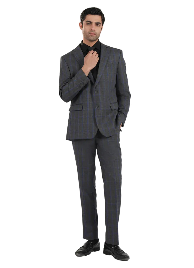 A man modeling a dark gray two-piece suit with a subtle blue and brown windowpane plaid pattern, paired with a black shirt and black dress shoes, against a light gray studio background.